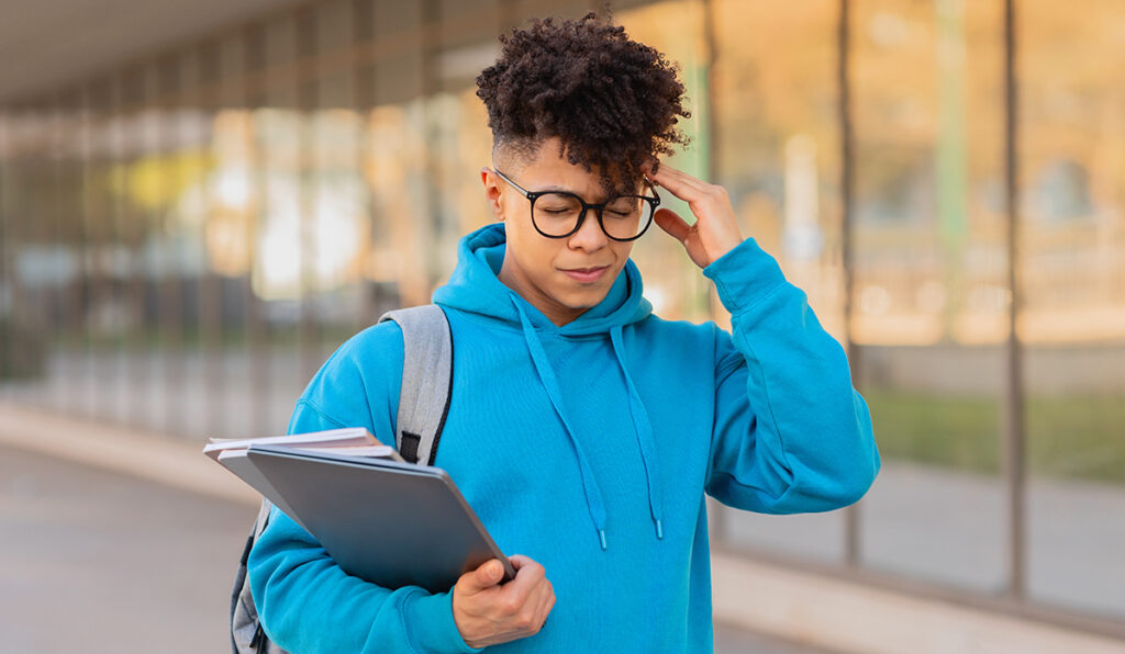 Introspective young brazilian guy student contemplates while holding a notebook and wearing a blue hoodie outdoors